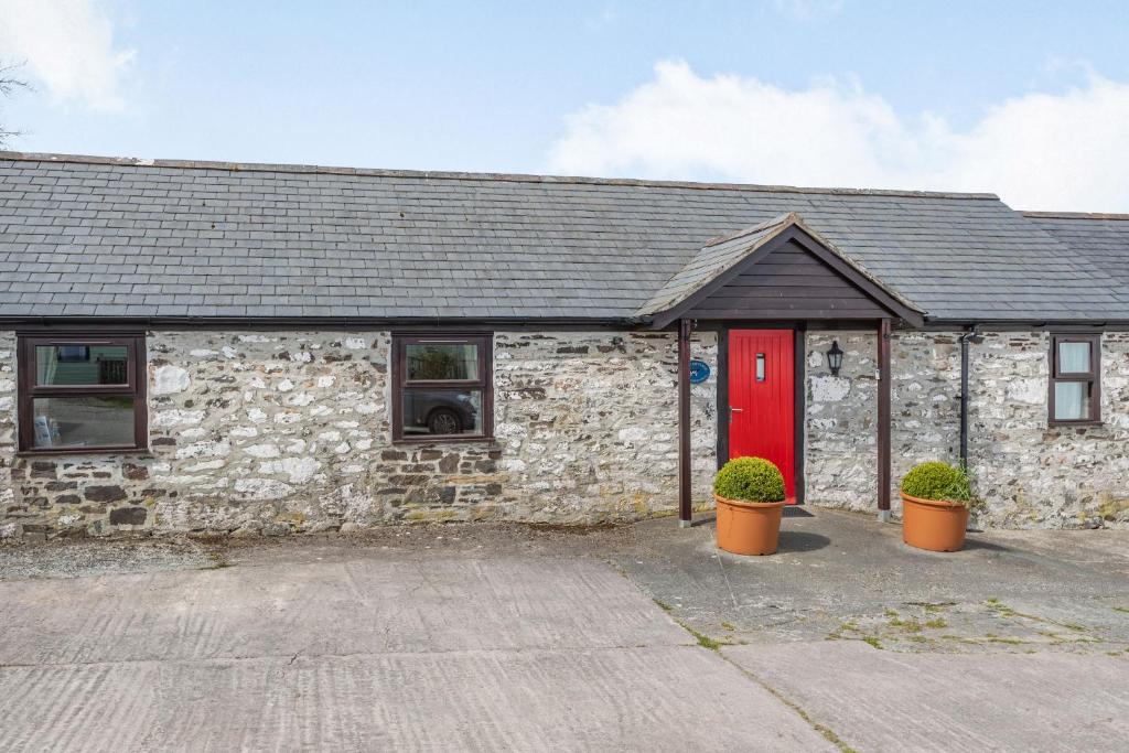 a stone building with a red door and two plants at Dairy Cottage in Llanrwst