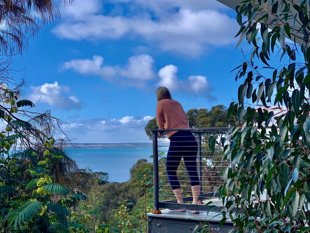 una donna in piedi su un balcone che guarda l'acqua di Sunrise on Falie Seaview Eco Accommodation ad American River