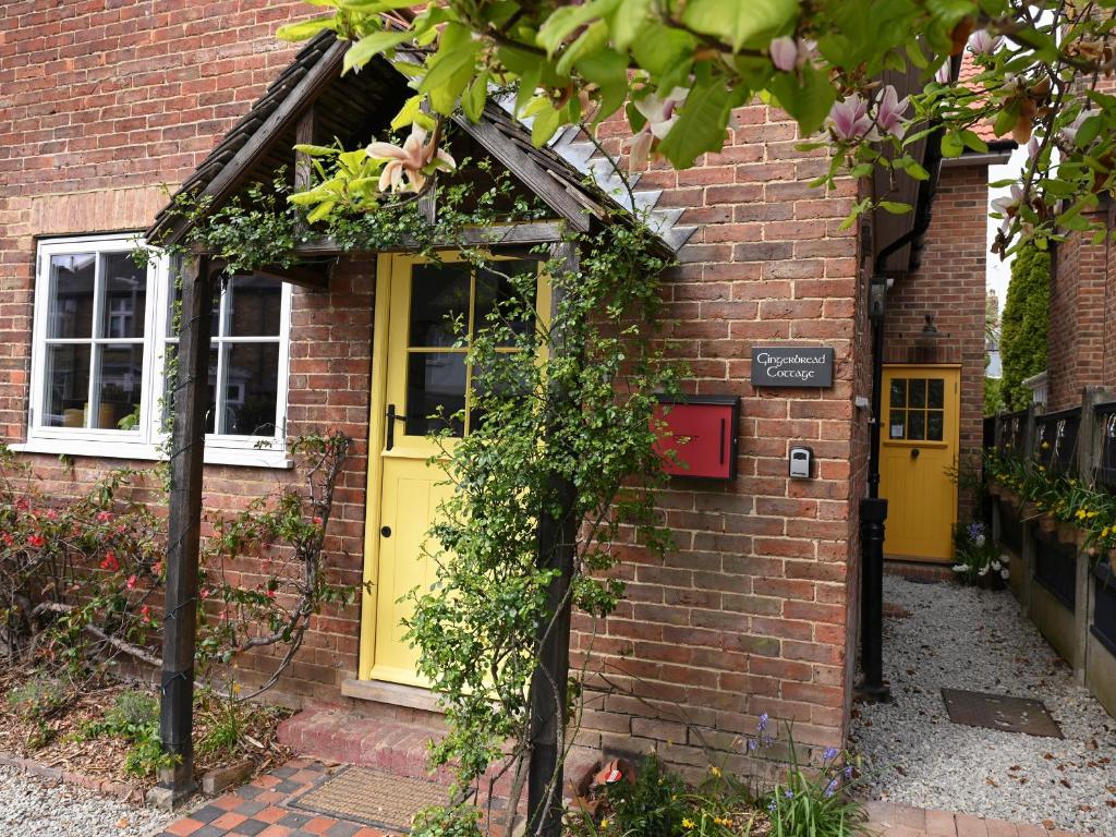 a brick building with a yellow door and flowers at Gingerbread Cottage in Canterbury