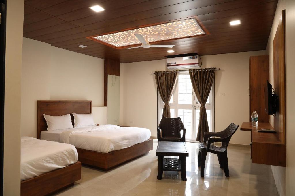 a bedroom with two beds and a table and a chair at Mahalaxmi Executive in Kolhapur