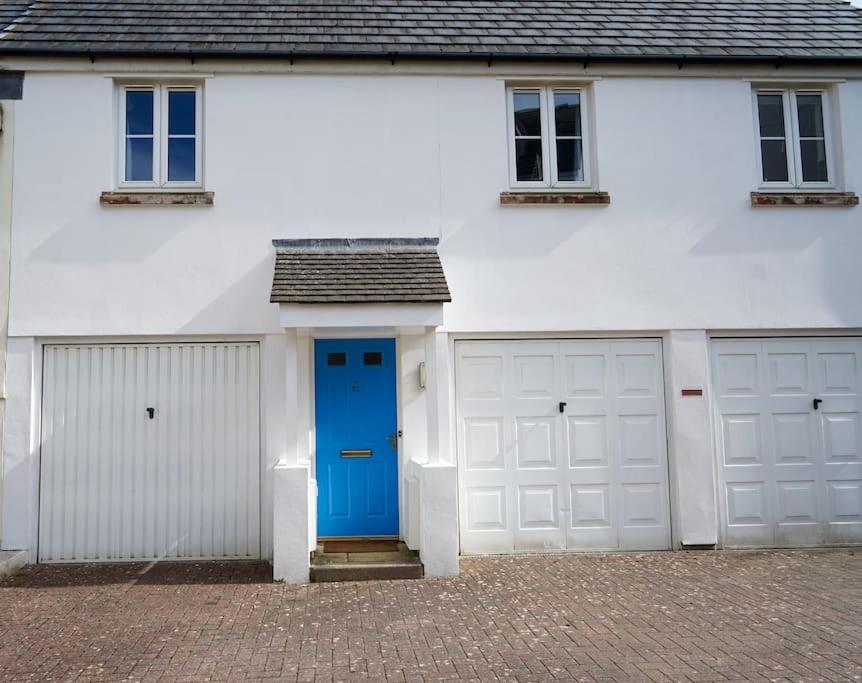 a white house with two garages and a blue door at The Coach House near Swanpool, Falmouth, Cornwall. in Falmouth