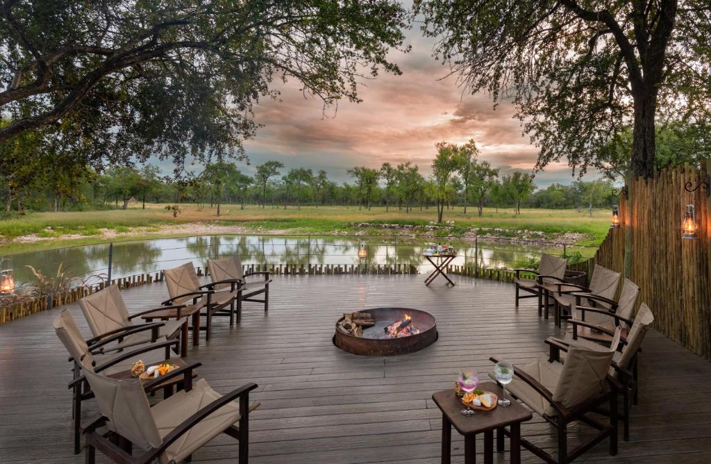 a deck with chairs and a fire pit next to a lake at Onguma Forest Camp in Namutoni