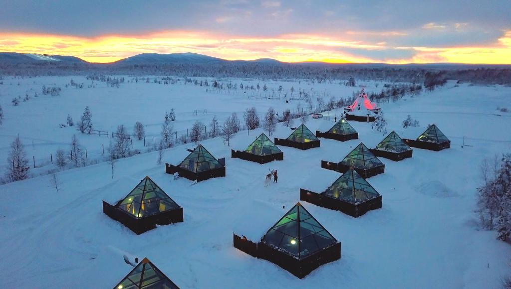 Aurora Pyramid Glass Igloos في Köngäs: مجموعة من النزل في الثلج عند غروب الشمس