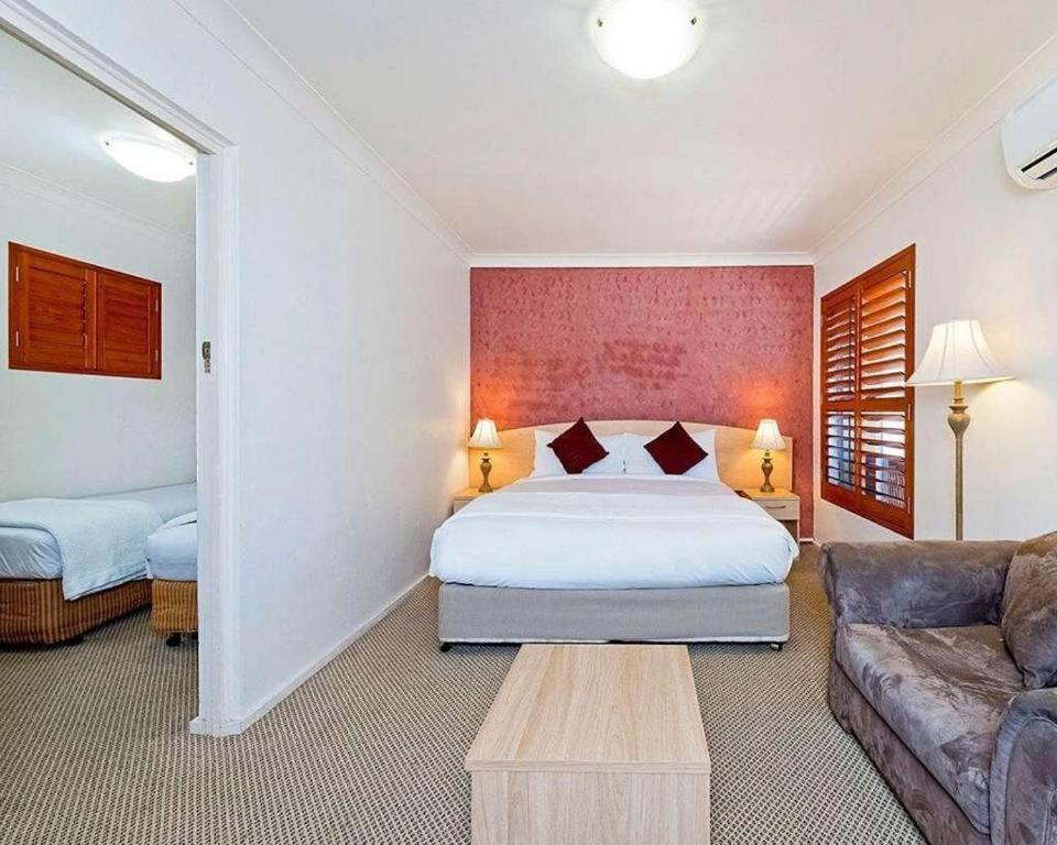 
a hotel room with a bed, chair, and nightstand at Country Plaza Motel Taree in Taree
