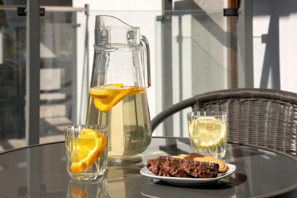 Pitcher of citrus water, two glasses and plate of chocolate biscuits on balcony table.