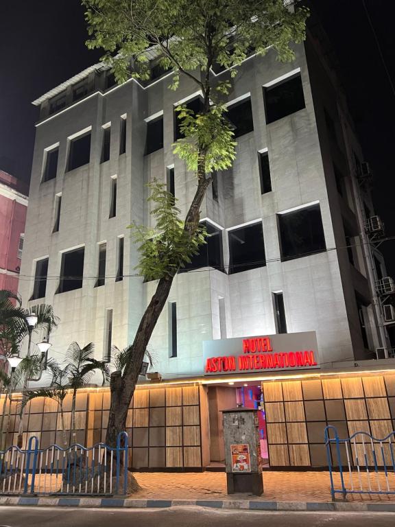 a white building with a tree in front of it at Hotel Aston International in Kolkata