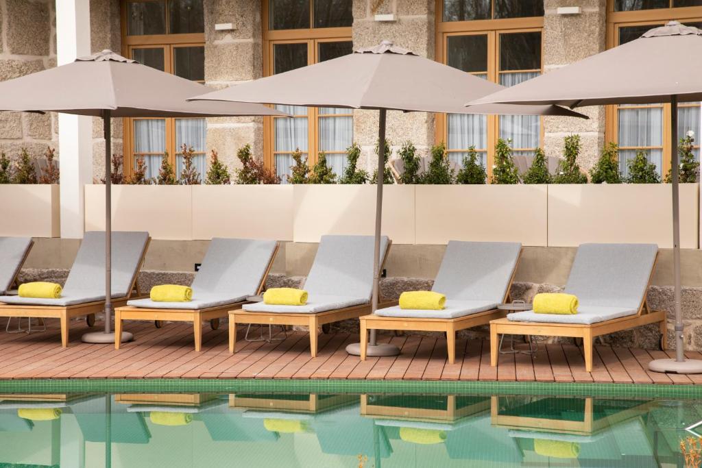 a row of lounge chairs with umbrellas next to a pool at Casa das Lérias in Amarante