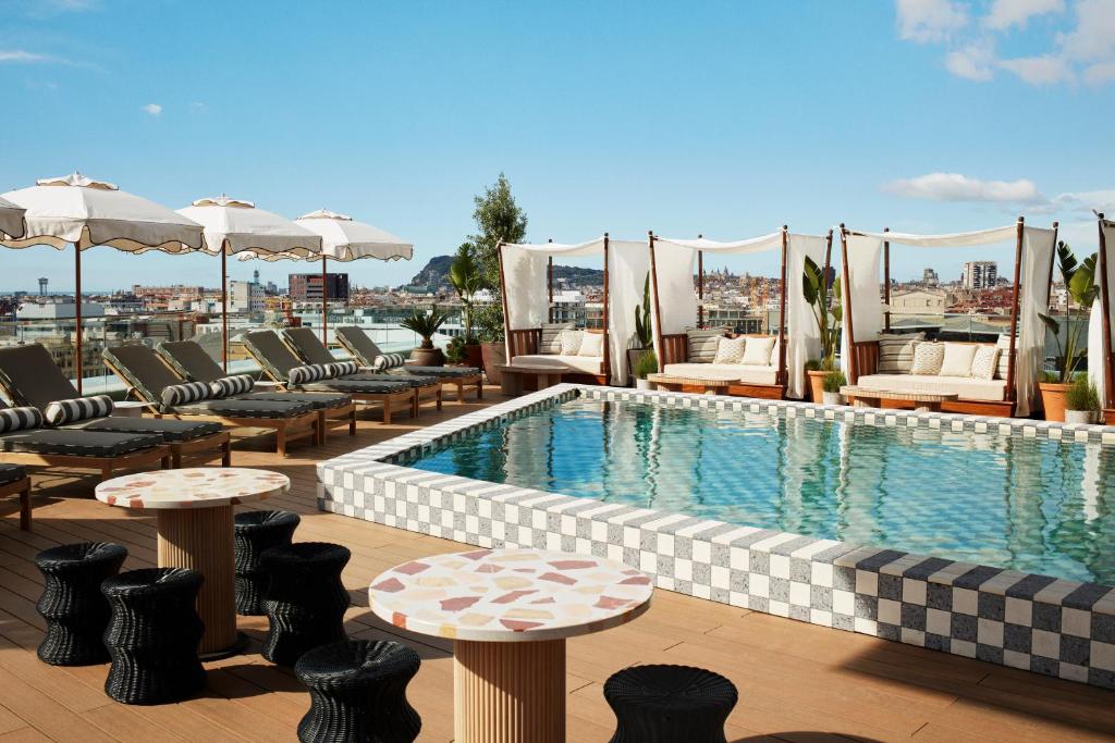 a pool on top of a building with chairs and tables at The Hoxton, Poblenou in Barcelona