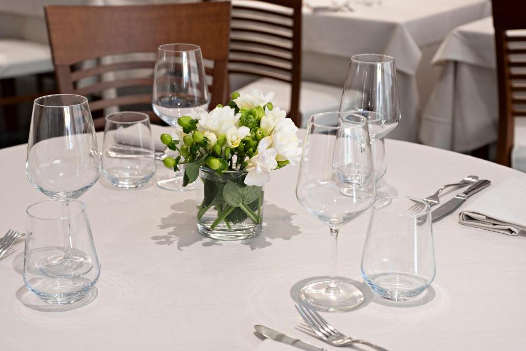 a table with wine glasses and a vase of white flowers at Hotel Mirage in Viareggio