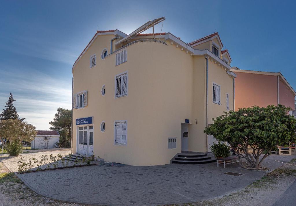 un grand bâtiment blanc avec un arbre en face dans l'établissement Apartments Dalmata, à Biograd na Moru