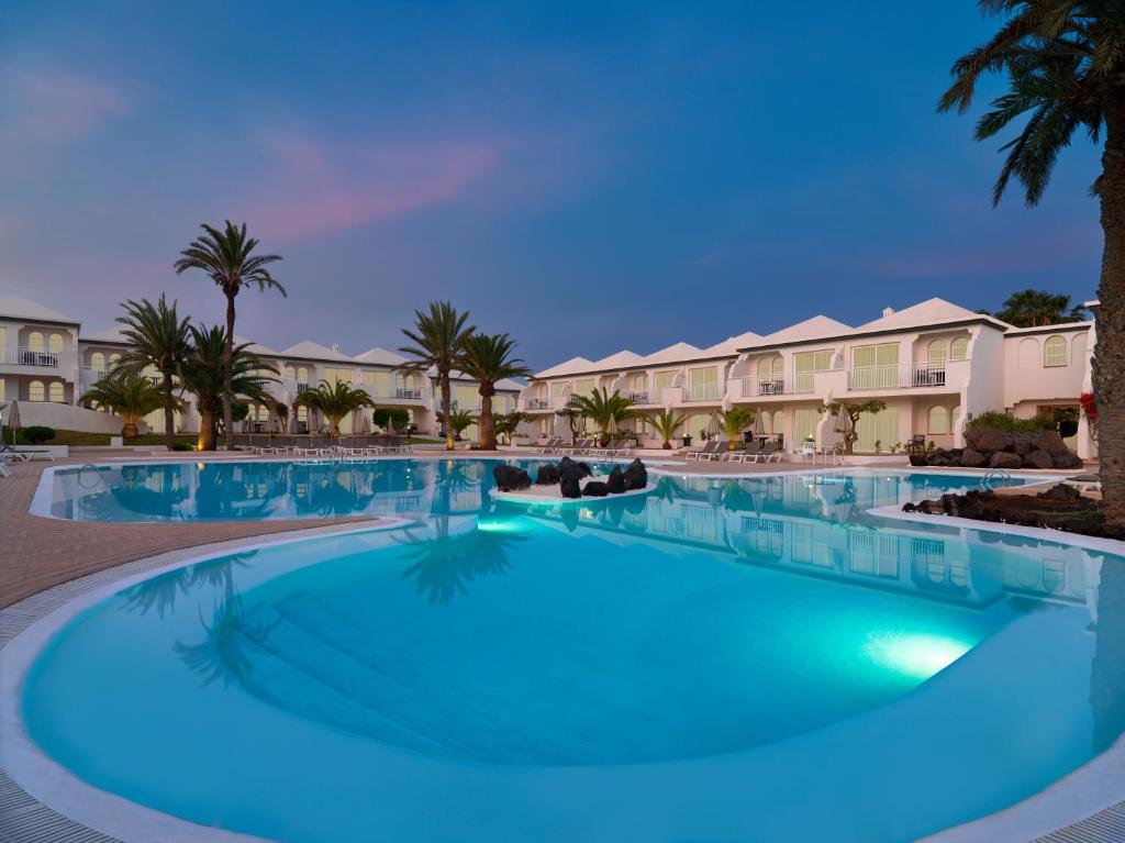a large swimming pool with palm trees and houses at H10 Ocean Suites in Corralejo