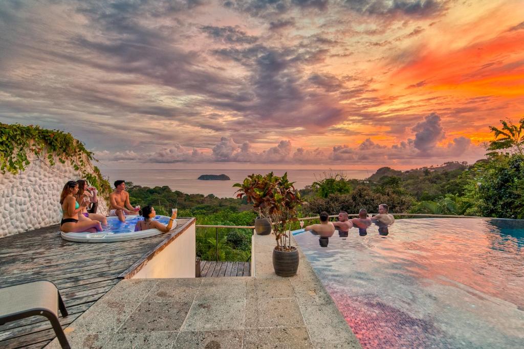 a group of people sitting next to a pool with a sunset at Villa Roca Boutique Resort & Suites - ADULT ONLY in Manuel Antonio