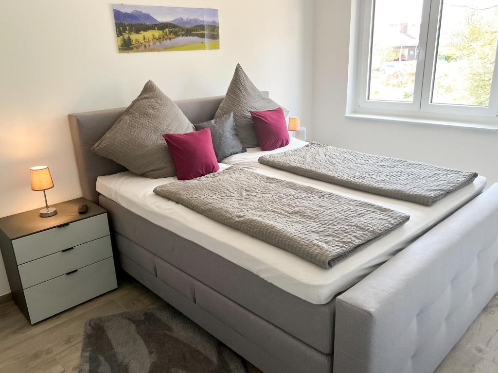 1 cama con almohadas rosas y grises y ventana en Wohnung Alpenblick en Höchenschwand