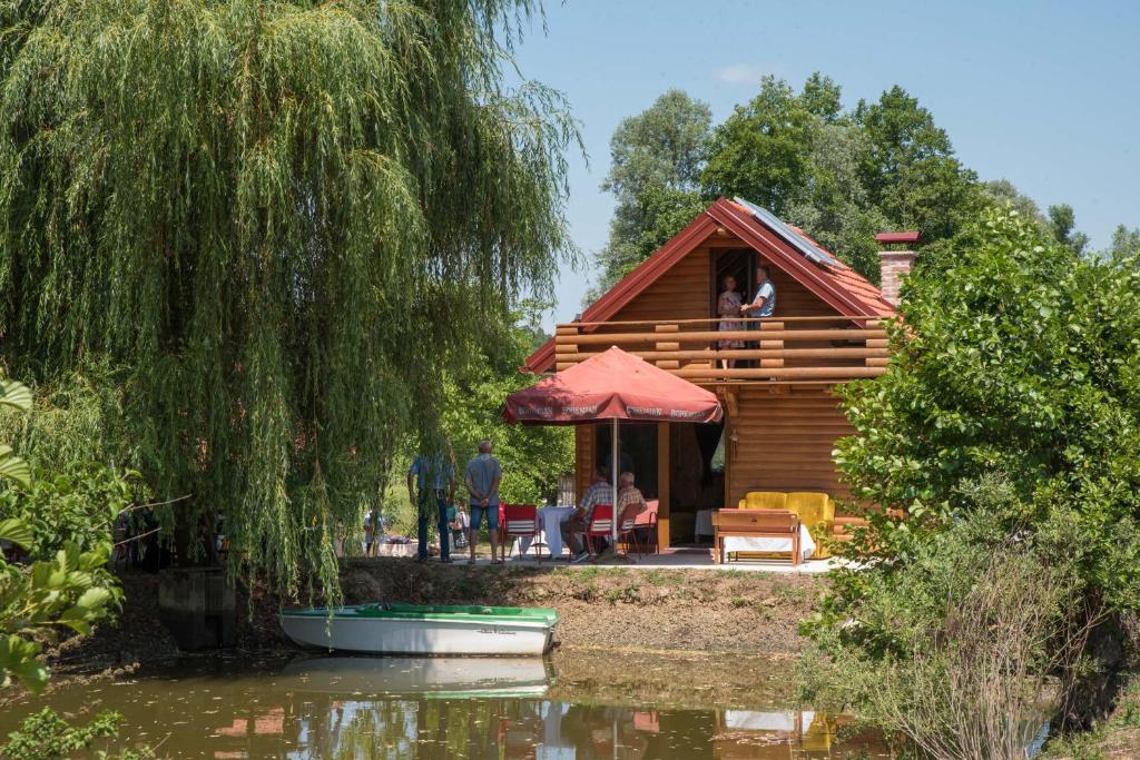 une cabane en rondins avec des personnes assises sur le pont à côté de l'eau dans l'établissement Robinzonski smještaj Oaza mira, à Končanica
