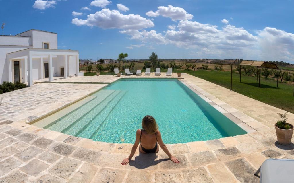 una mujer sentada frente a una piscina en Masseria Rifisa AgriResort, en Caprarica di Lecce