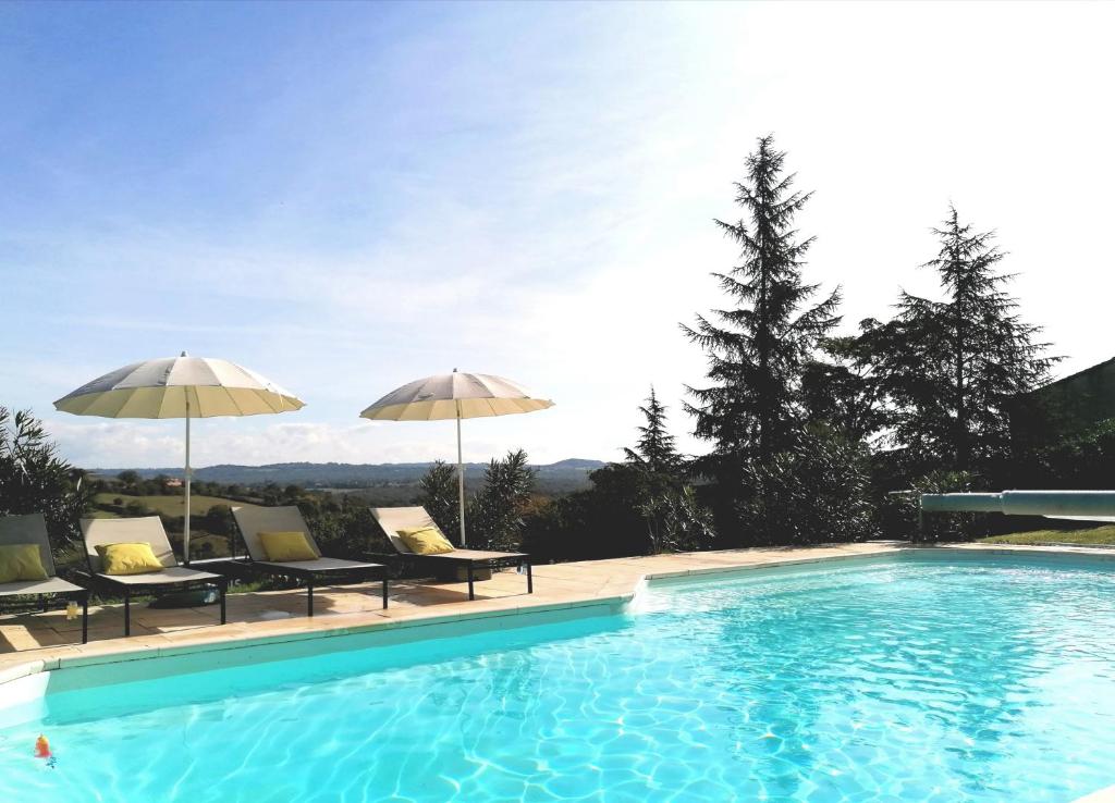 a swimming pool with two umbrellas and some chairs at Le Mas de Coline in Rocamadour
