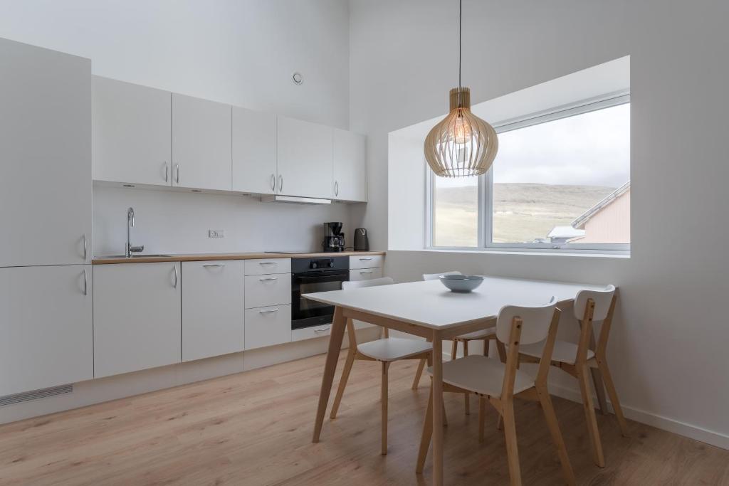 cocina con armarios blancos, mesa y sillas en Brand New / Airport / RentYourCar / Free Parking, en Miðvágur