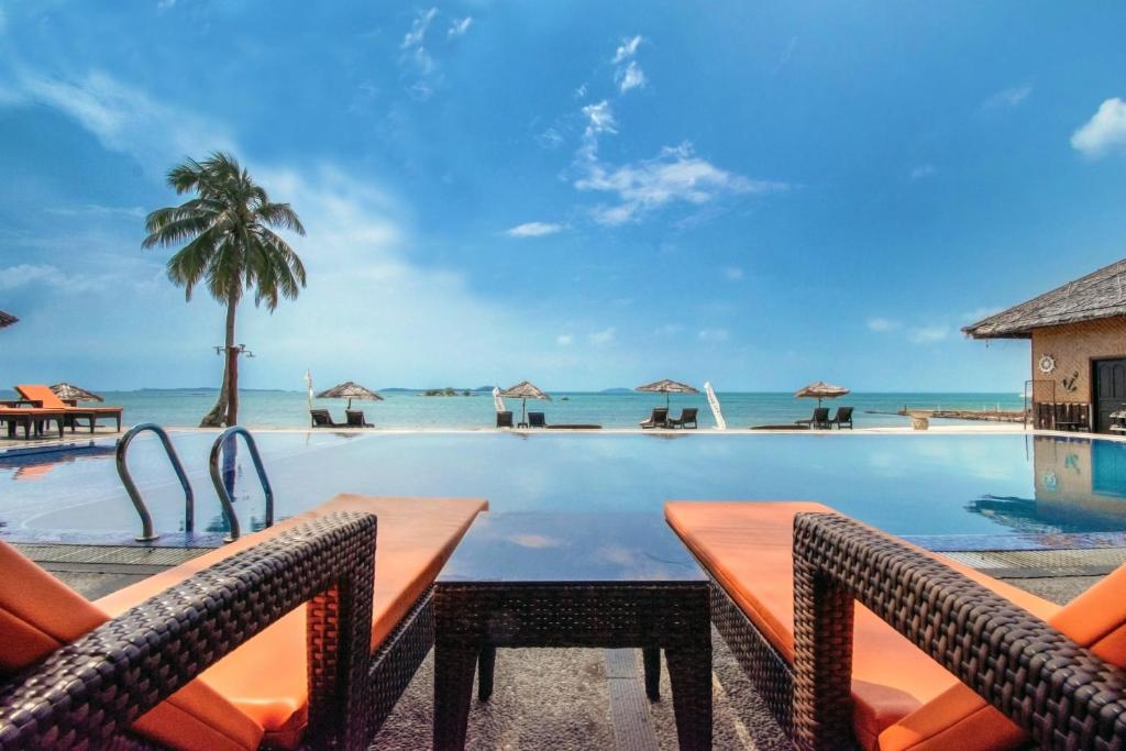 einen Pool mit Stühlen und das Meer im Hintergrund in der Unterkunft Bintan Spa Villa Beach Resort & Spa in Teluk Bakau