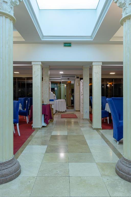 a hall with columns and tables and blue chairs at Hotel Grand in Eforie Nord