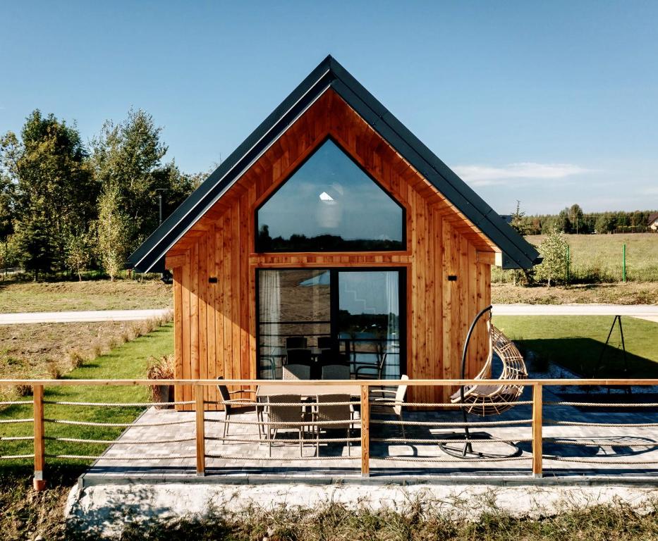 Front-facing wood cabin with large triangular window, patio dining set and hanging swing chair.