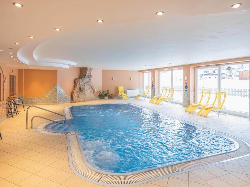 a large swimming pool in a hotel room with yellow chairs at Hotel Styrolerhof in Steeg