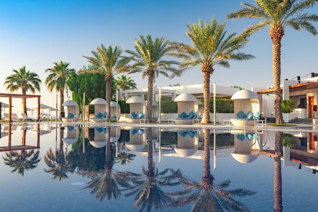 a resort pool with palm trees and buildings at Sealine Beach, a Murwab Resort in Mesaieed