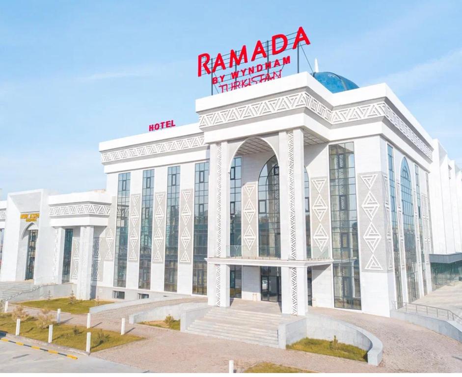 a white building with a sign on top of it at Ramada by Wyndham Turkistan in Türkistan