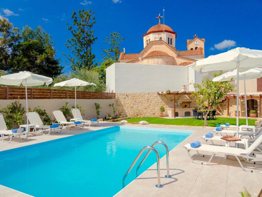 a pool with chairs and umbrellas in front of a building at Villa Lucas in Melidhónion