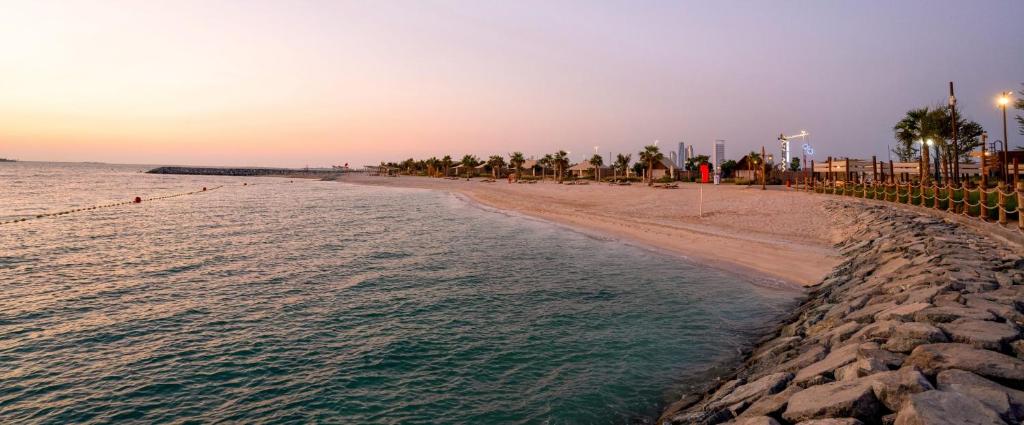 uma praia com palmeiras e o oceano ao pôr do sol em Bab Al Nojoum Hudayriyat Camp em Abu Dhabi