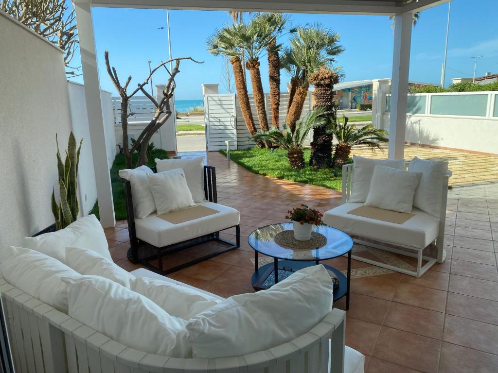 un patio con sofás blancos, una mesa y palmeras en Villa Mare Ibleo, en Marina di Ragusa