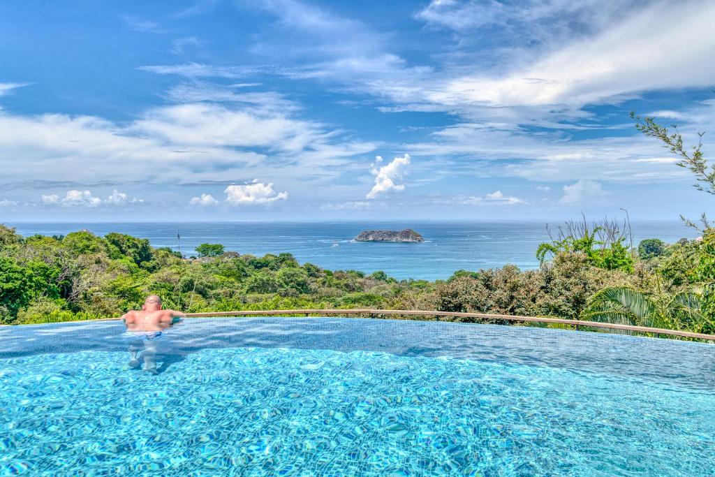 a man in a swimming pool overlooking the ocean at Villa Roca Boutique Resort & Suites - ADULT ONLY in Manuel Antonio