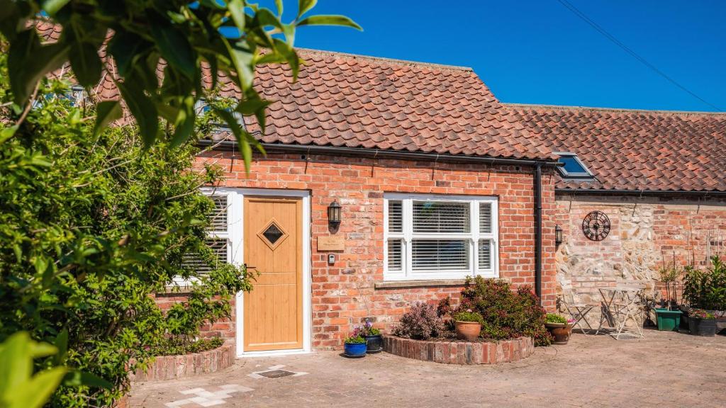a brick house with a orange door and some plants at The Old Milking Parlour in Barmston