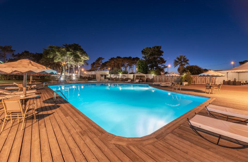 a swimming pool at night with chairs and umbrellas at Hotel Vale Da Telha in Aljezur