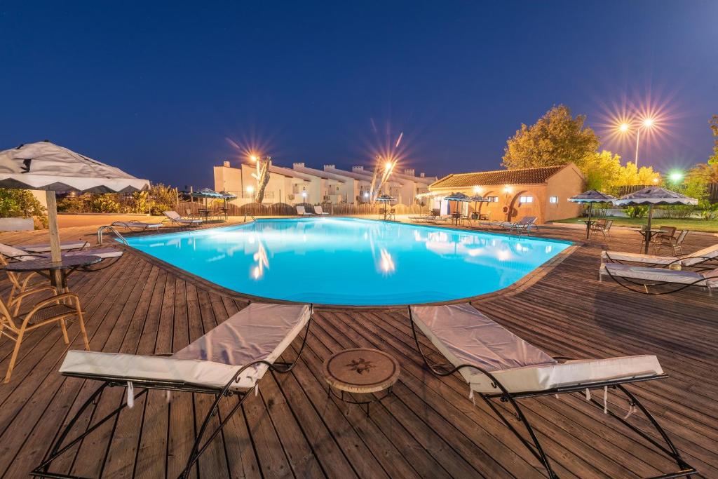 a large swimming pool with chairs and umbrellas on a deck at Hotel Vale Da Telha in Aljezur