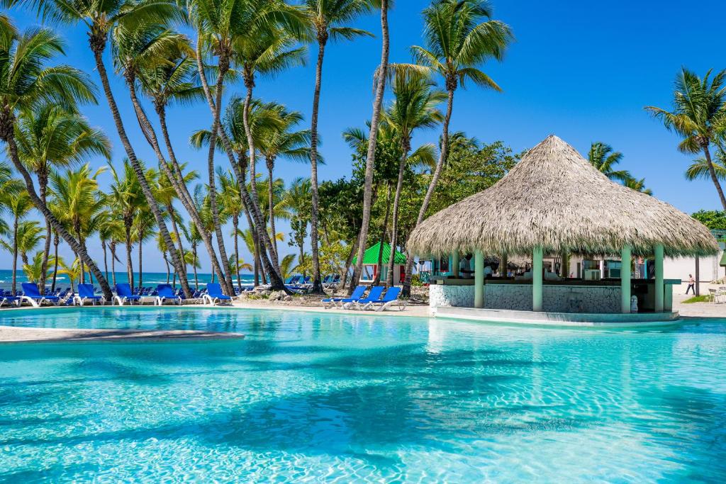 a swimming pool with palm trees and a hut at Coral Costa Caribe Beach Resort - All Inclusive in Juan Dolio