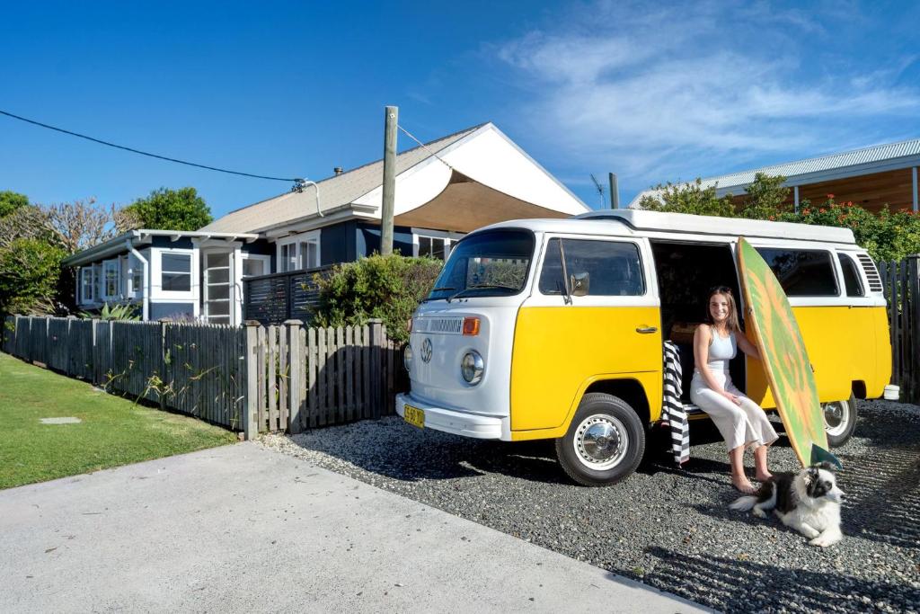 a woman sitting next to a yellow and white van with a surfboard at Avalon vintage beachside family getaway in Currarong