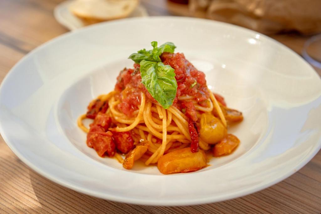 a white plate of pasta with sauce and a garnishment at Cala Cala Rooms,Restaurant & Farm Experience in Procida