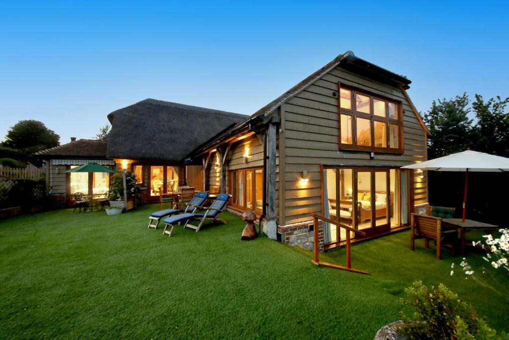 a house with a yard with chairs and an umbrella at A Barn at South Downs Stay in Houghton