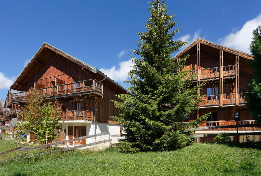 un grand bâtiment avec un arbre devant dans l'établissement Résidence Néméa Les Chalets Des Cîmes, à La Toussuire