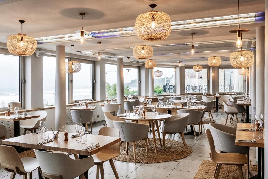 a restaurant with tables and chairs and windows at Hôtel Le Windsor Biarritz in Biarritz