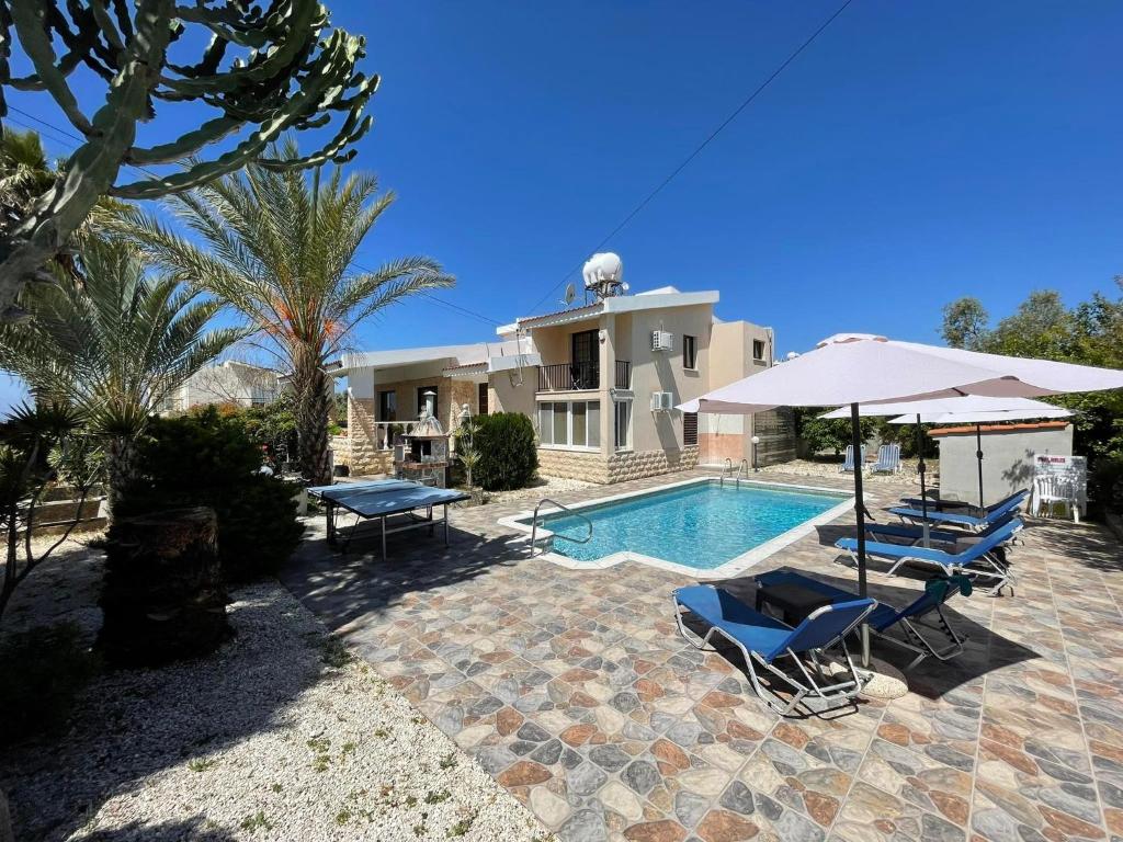 a house with a swimming pool and two chairs and an umbrella at Villa Ocean Stones 1Km From Main Coral Bay Beach in Peyia