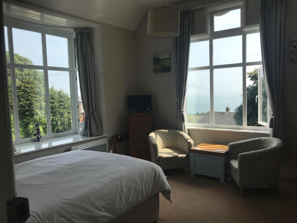 a bedroom with a bed and two chairs and windows at Cornerways in Ventnor