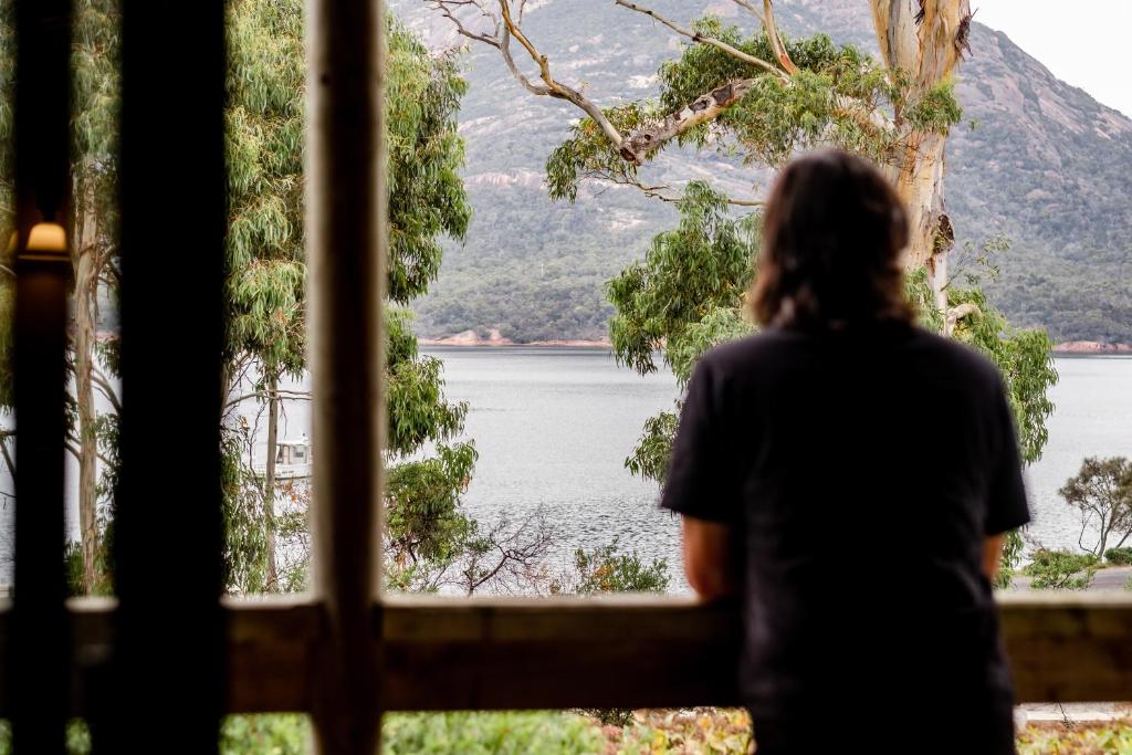 a woman looking out of a window at a lake at Freycinet Cottage 1 – Bluestone in Coles Bay