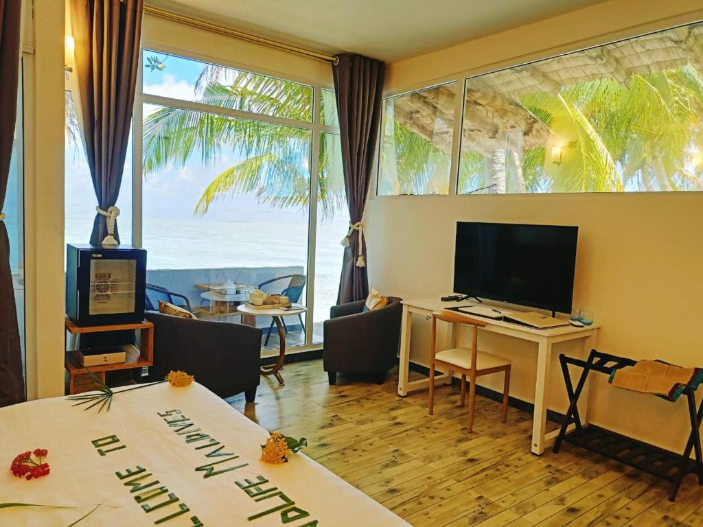 a hotel room with a desk with a television and a view of the ocean at Island Life Maldives Retreat & Spa in Magoodhoo