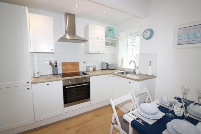 a kitchen with white cabinets and a table with a dining room at Beachcomber Cottage in Troon