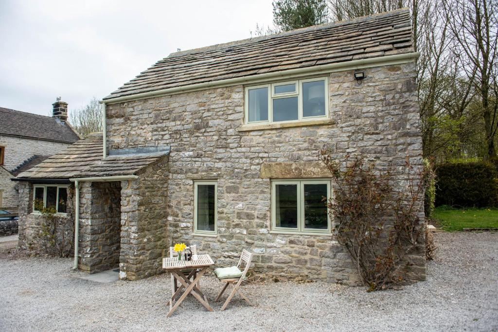 a stone house with a table and a chair in front of it at Brosterfield Cottage in Foolow