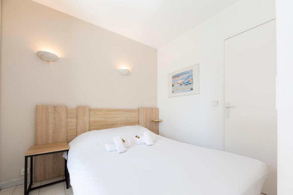 a white bedroom with a bed and a wooden headboard at 1 bedroom apartment in a residence with a swimming pool and a parking spot in Vallauris