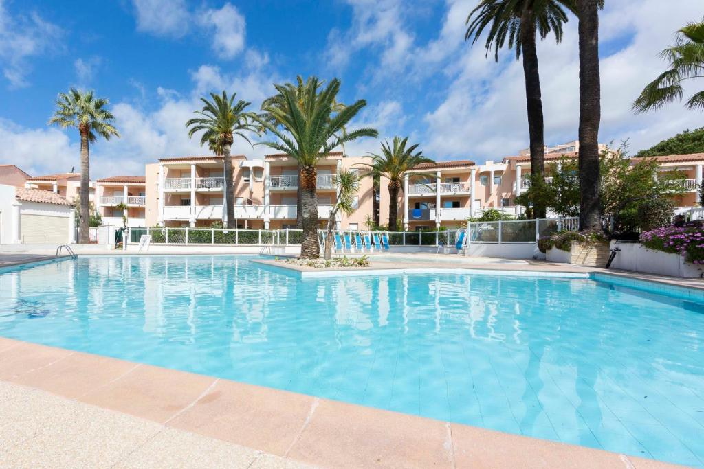 a large swimming pool with palm trees in front of a building at 1 bedroom apartment in a residence with a swimming pool and a parking spot in Vallauris