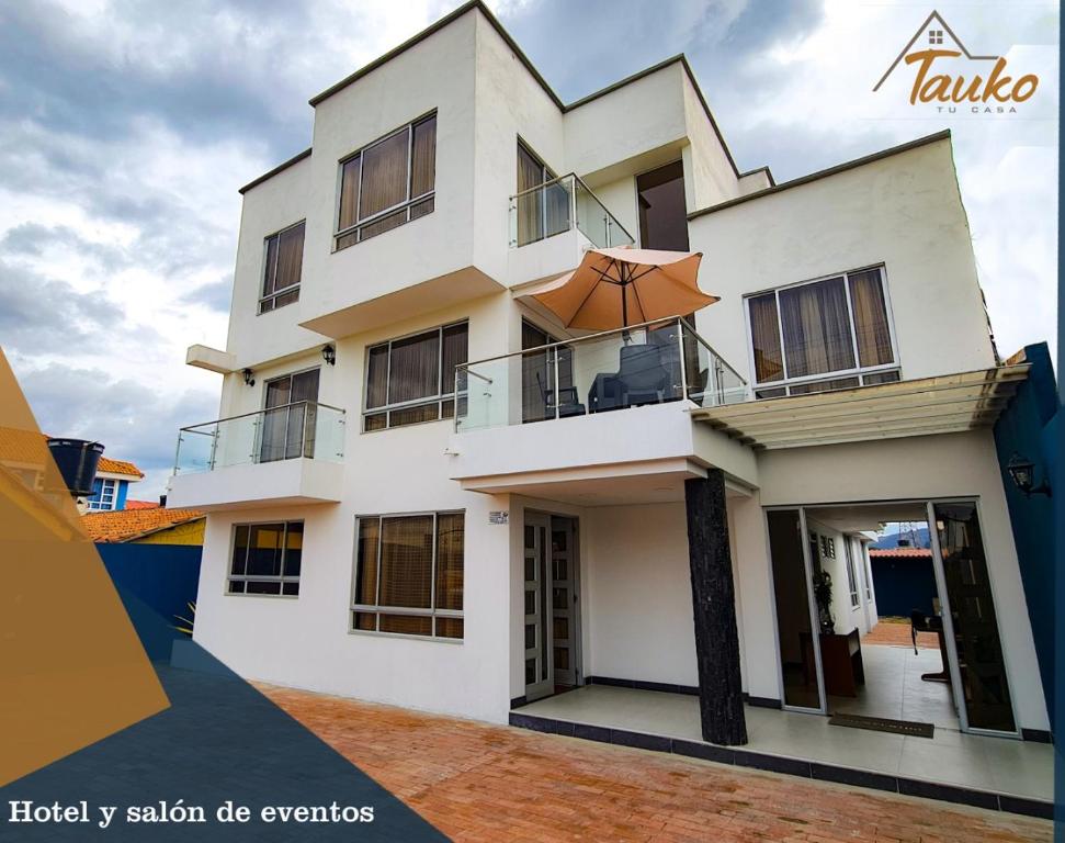 uma casa branca com um guarda-chuva na varanda em Tauko tu casa em Paipa