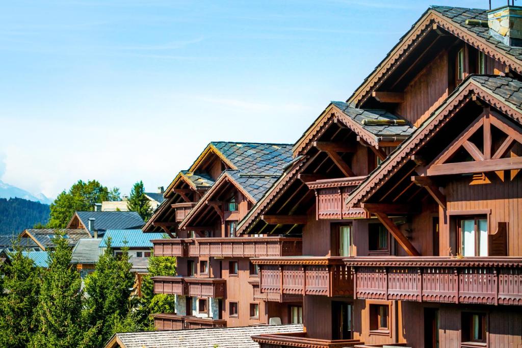a group of wooden buildings with mountains in the background at Résidence Pierre & Vacances Premium Les Fermes De Méribel in Méribel